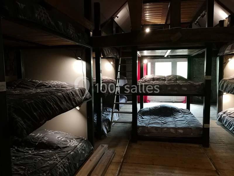 Dortoir avec lits superposés en bois, éclairage tamisé et fenêtre laissant entrer la lumière naturelle.