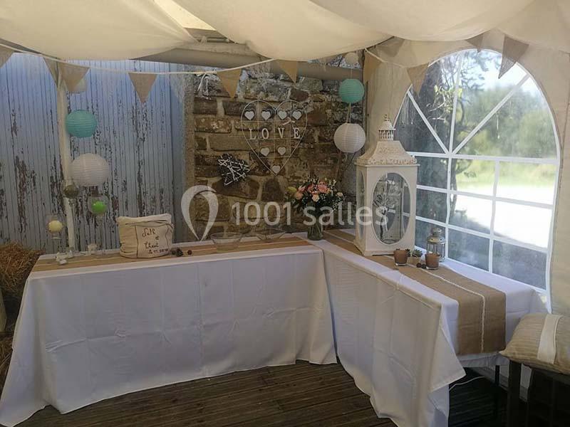 Décoration de mariage rustique avec table drapée, lanternes, guirlandes et fleurs dans une tente lumineuse.