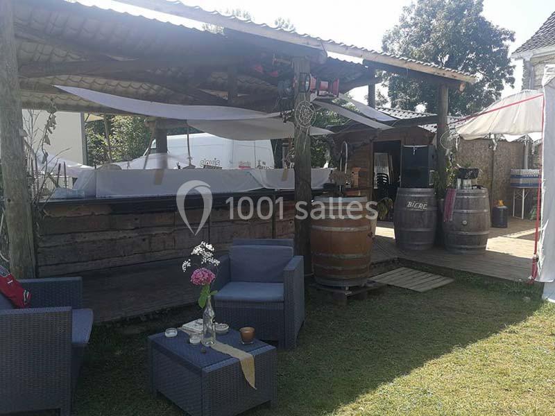 Espace extérieur aménagé avec des fauteuils, des tonneaux en bois et un comptoir sous un abri en bois.