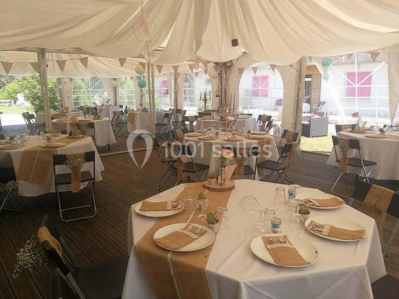 Intérieur d'une tente de réception décorée avec des tables rondes dressées et des éléments champêtres.