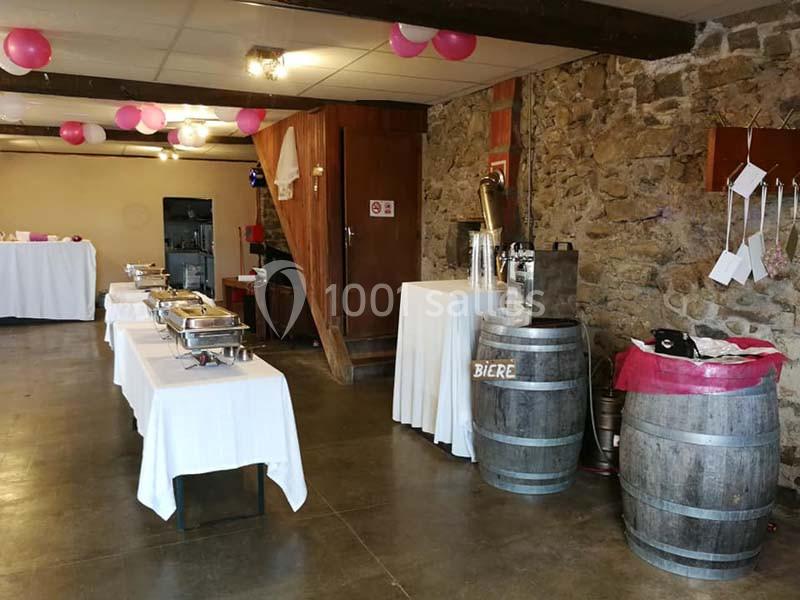 Salle décorée avec des ballons roses et blancs, tables de buffet dressées et tonneaux utilisés comme supports.