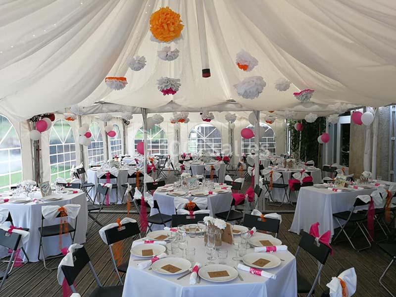 Salle de réception sous chapiteau décorée de guirlandes et tables dressées avec nappes blanches et accents roses.