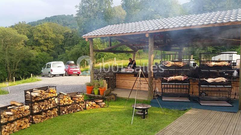 Barbecue en plein air sous un abri en bois, avec des porcelets rôtissant sur des grilles et des bûches empilées à proximité.