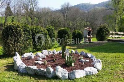 Aménagement de jardin avec un parterre circulaire entouré de pierres, contenant des plantes, sur fond de verdure et collines.