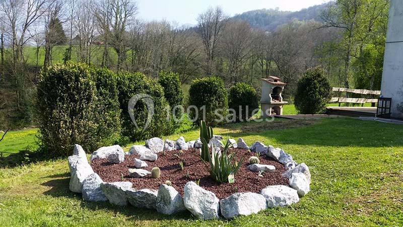 Aménagement de jardin avec un parterre circulaire entouré de pierres, contenant des plantes, sur fond de verdure et collines.