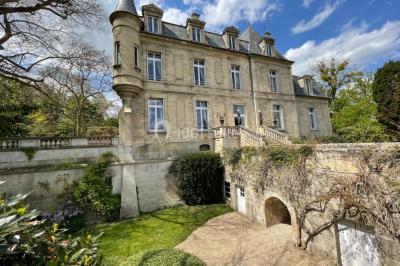 Façade d'un bâtiment en pierre de style classique avec tourelle, entouré d'une grille en fer forgé et d'un jardin.