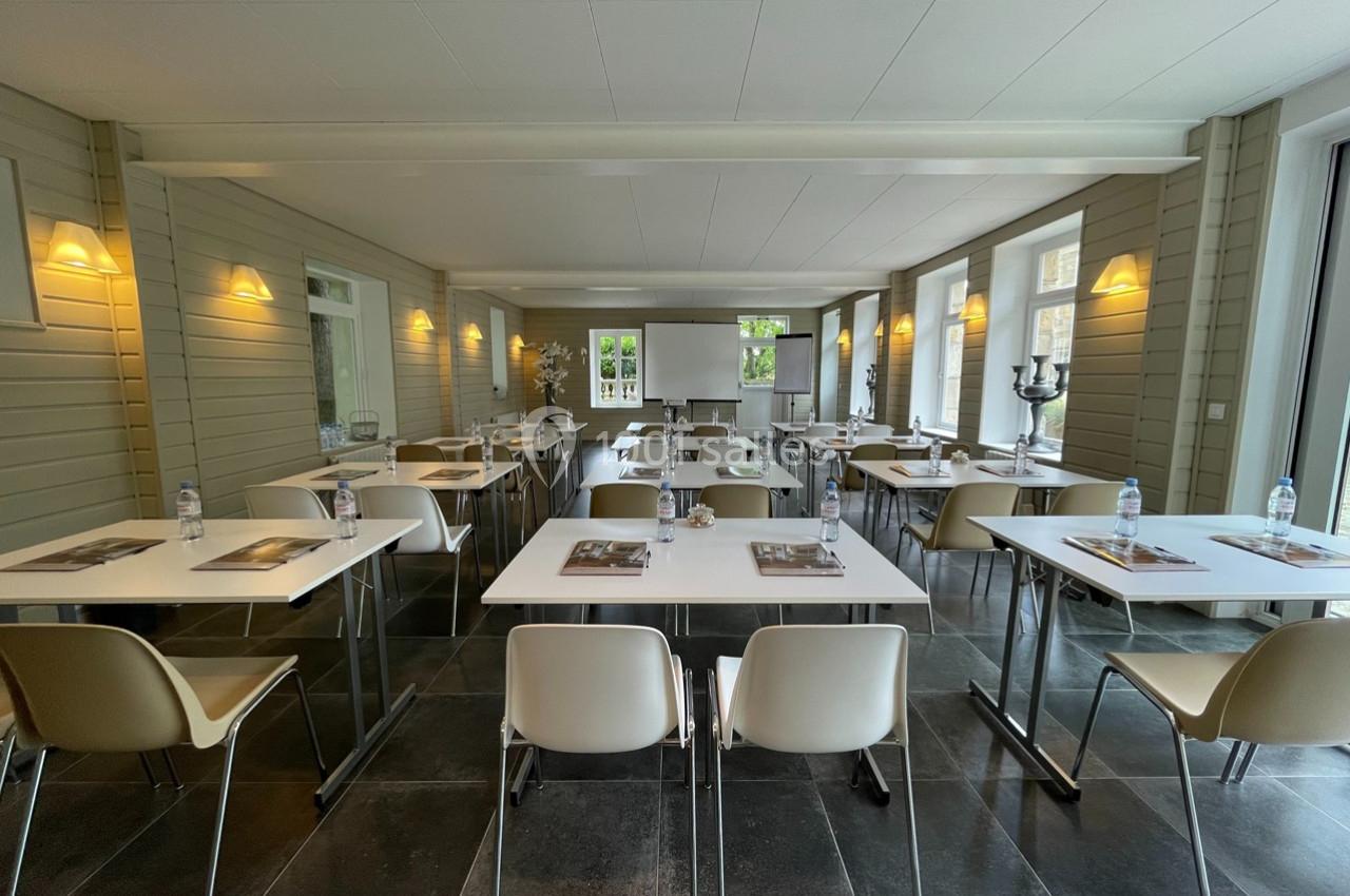 Salle lumineuse aménagée avec des tables et chaises, prête pour une réunion ou un repas, avec des bouteilles d'eau disposées.
