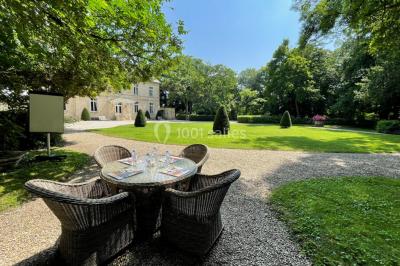 Façade d'un bâtiment en pierre de style classique avec tourelle, entouré d'une grille en fer forgé et d'un jardin.