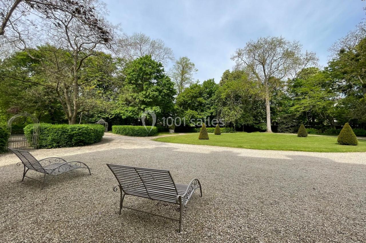 Deux chaises longues en métal sur une allée gravillonnée, entourées de pelouse et d'arbres dans un jardin paisible.