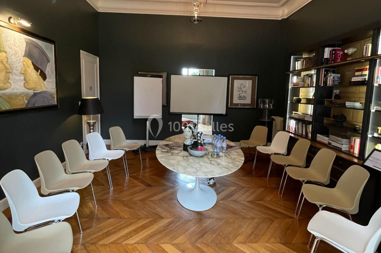Salle de réunion avec table ronde en marbre, chaises disposées en cercle, tableau blanc et étagères remplies de livres.