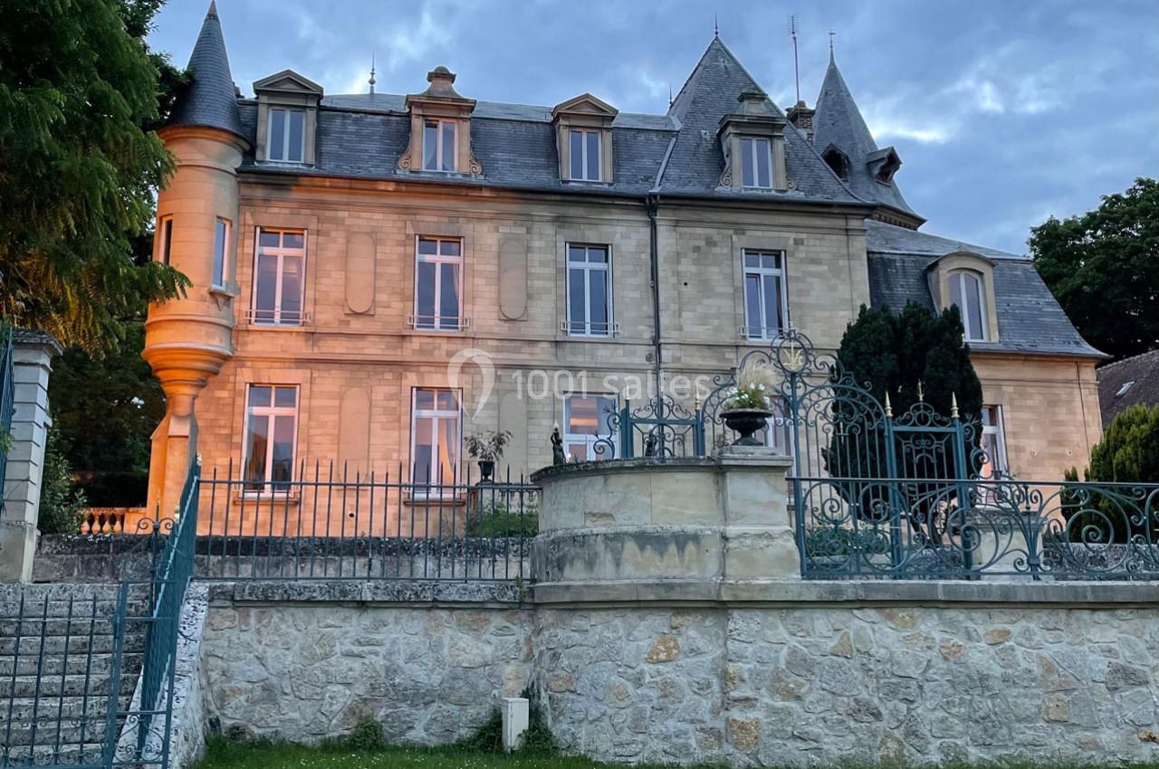 Façade d'un bâtiment en pierre de style classique avec tourelle, entouré d'une grille en fer forgé et d'un jardin.