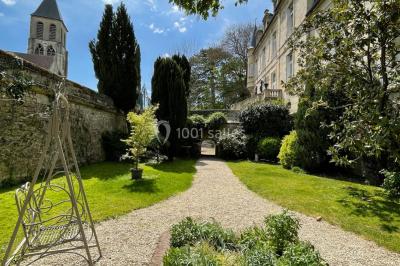 Façade d'un bâtiment en pierre de style classique avec tourelle, entouré d'une grille en fer forgé et d'un jardin.