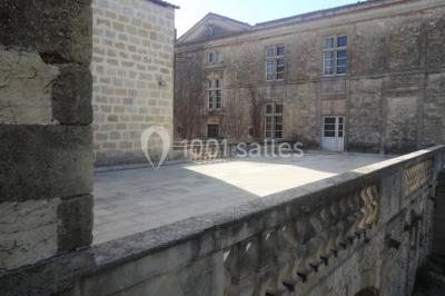 Terrasse en pierre spacieuse devant un bâtiment ancien en pierre sous un ciel bleu dégagé.