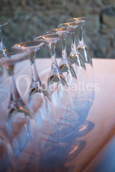 Rangée de verres à pied retournés alignés sur une nappe blanche, avec un mur en pierre en arrière-plan.