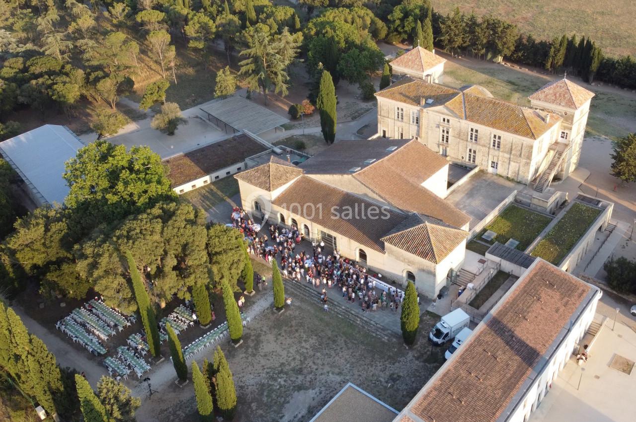 Vue aérienne d'un domaine avec bâtiments anciens, une cour animée par un rassemblement et des tables dressées en extérieur.