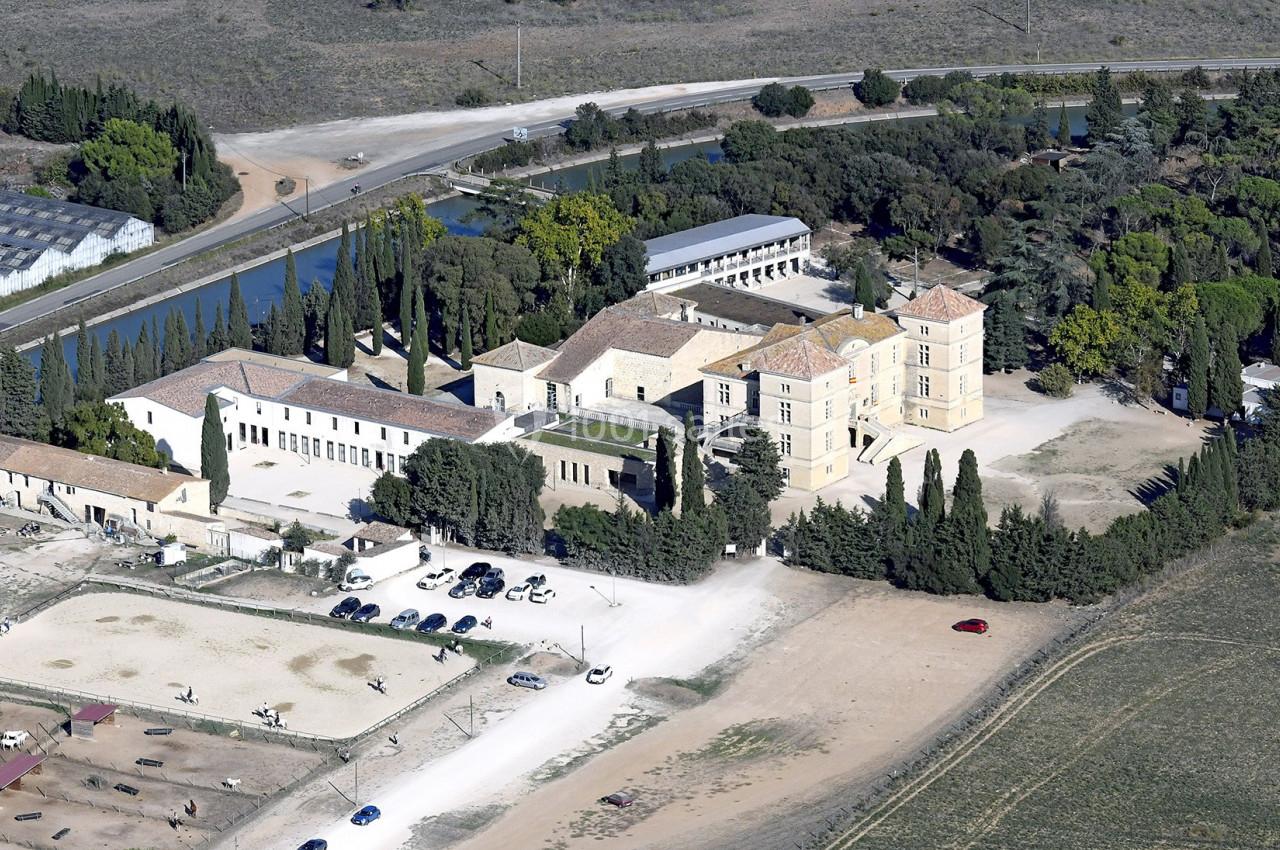 Vue aérienne d'un domaine avec un grand bâtiment principal, des annexes, un canal et des espaces verts environnants.
