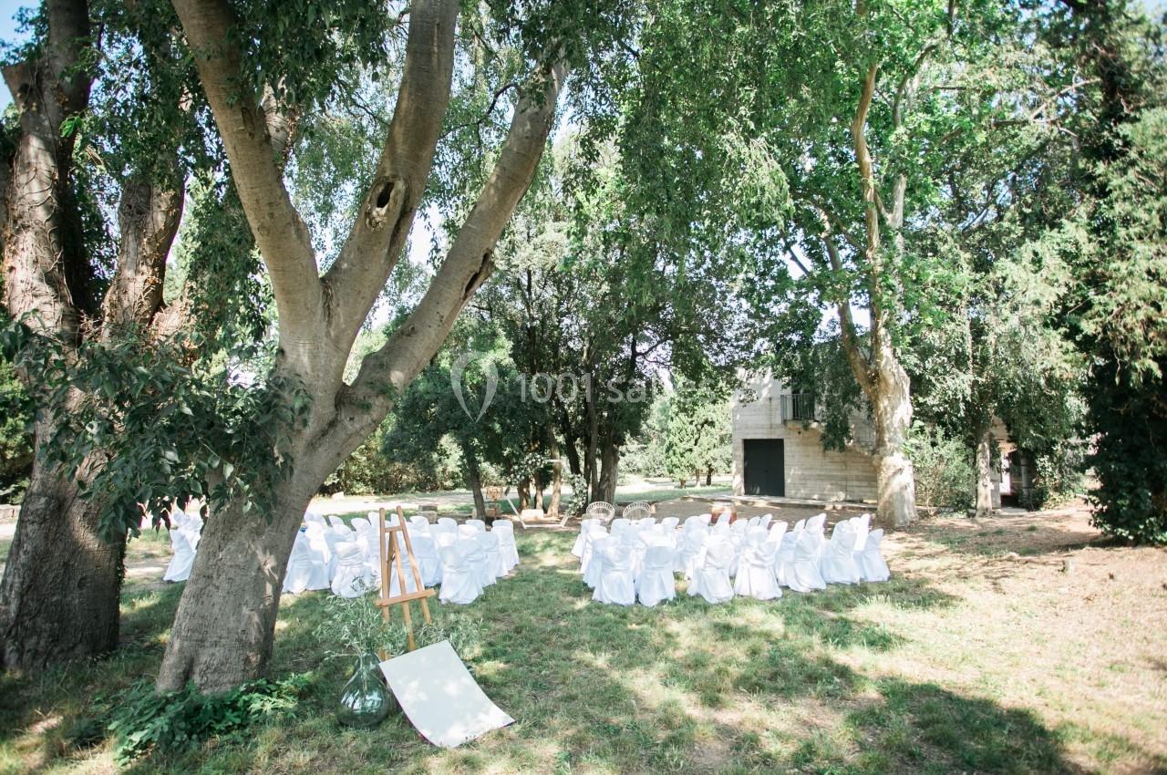 Chaises blanches disposées en cercle sous des arbres dans un jardin verdoyant, avec un chevalet au premier plan.