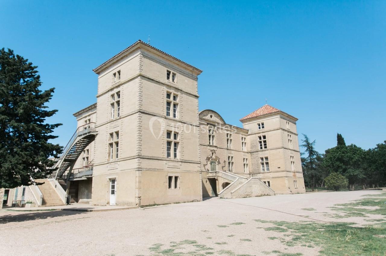 Façade d'un château en pierre avec deux tours carrées, entouré d'arbres sous un ciel bleu clair.