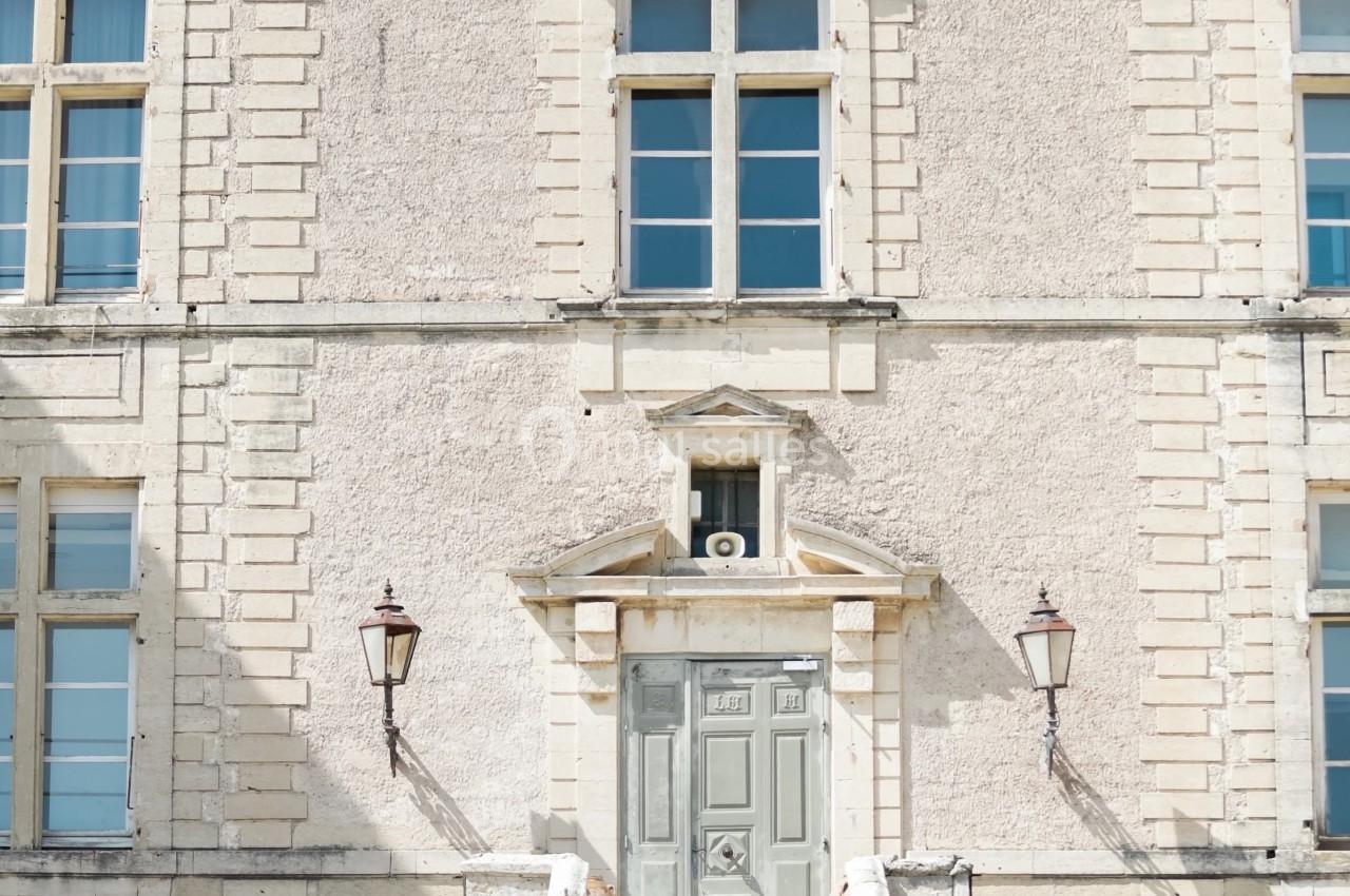 Façade d'un bâtiment ancien en pierre avec une porte centrale, des fenêtres symétriques et deux lanternes murales.
