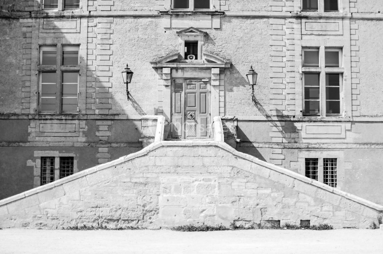 Façade d'un bâtiment ancien avec une porte centrale, deux lampadaires et un escalier en pierre symétrique.