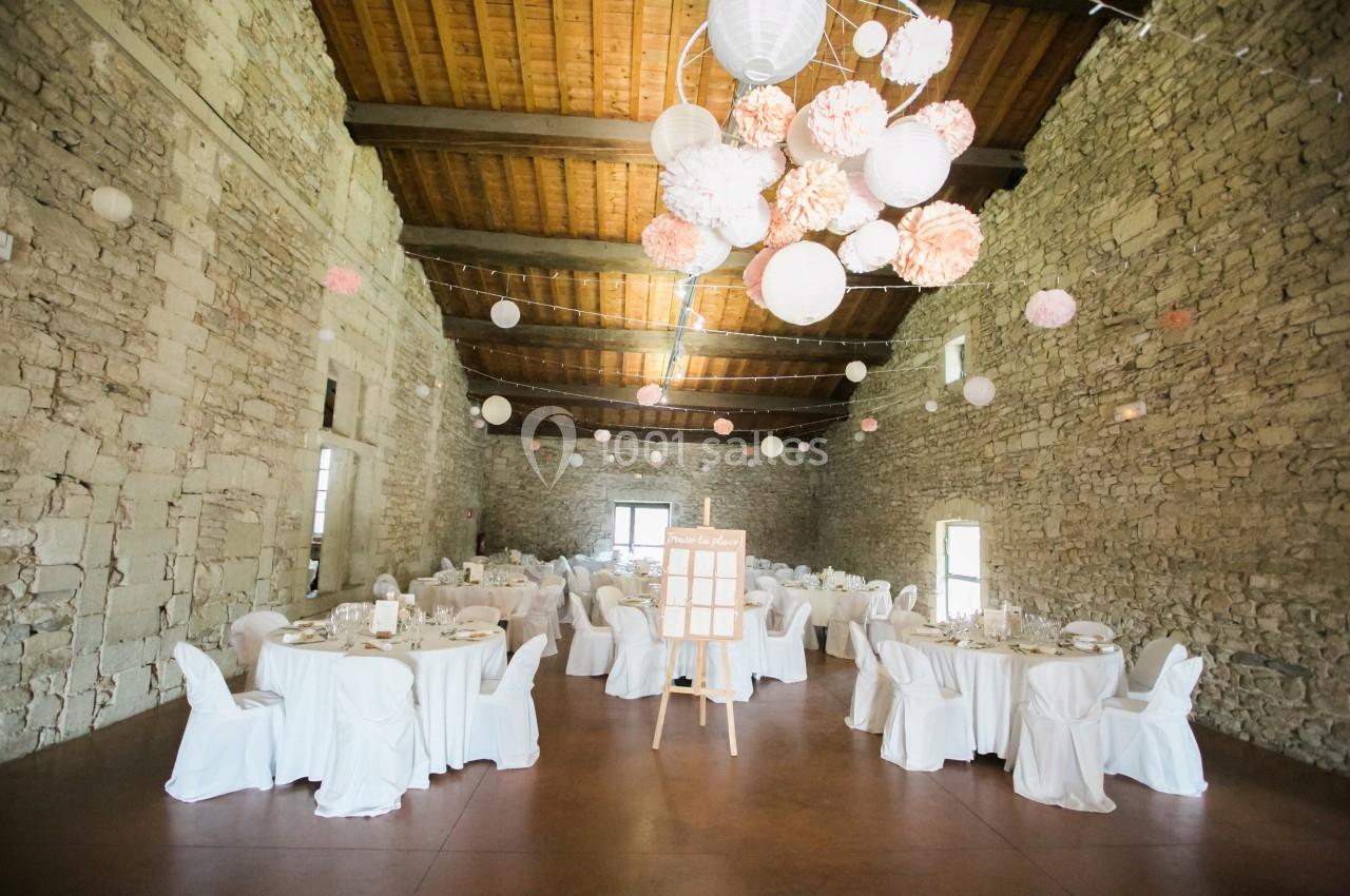 Salle en pierre avec tables rondes dressées pour un événement, décorée de lanternes et pompons suspendus au plafond.