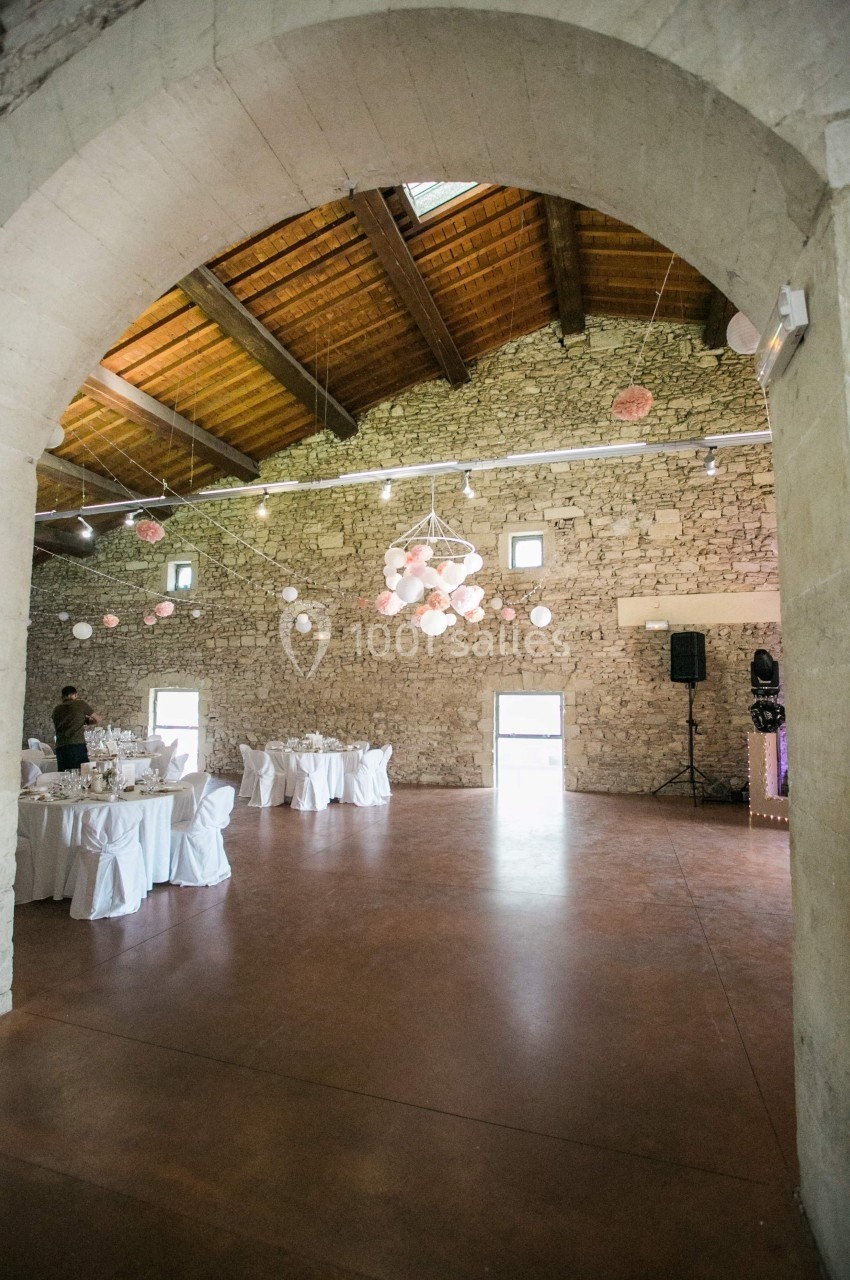 Salle en pierre avec plafond en bois, décorée de guirlandes lumineuses et de lanternes, tables dressées pour un événement.