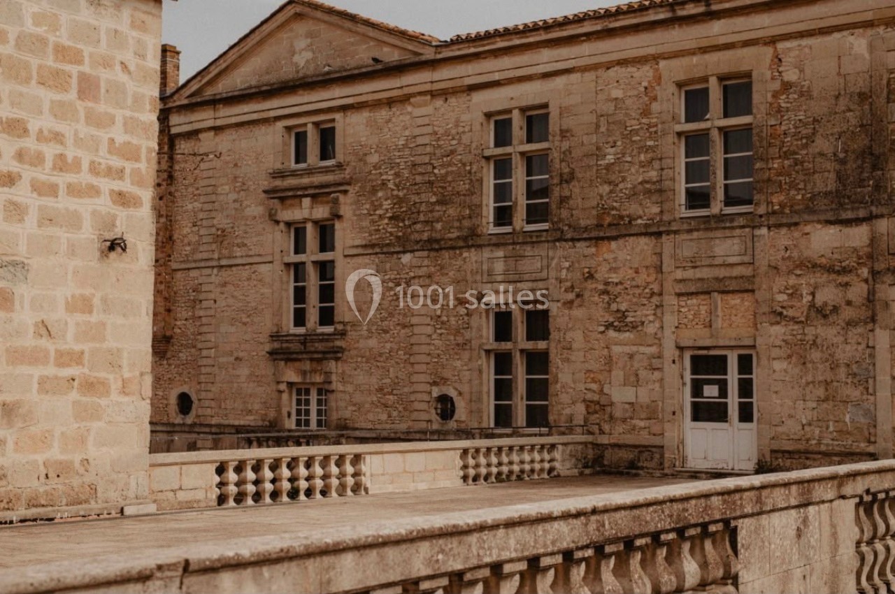 Façade en pierre d'un bâtiment ancien avec fenêtres à croisillons, vue depuis une balustrade en pierre.