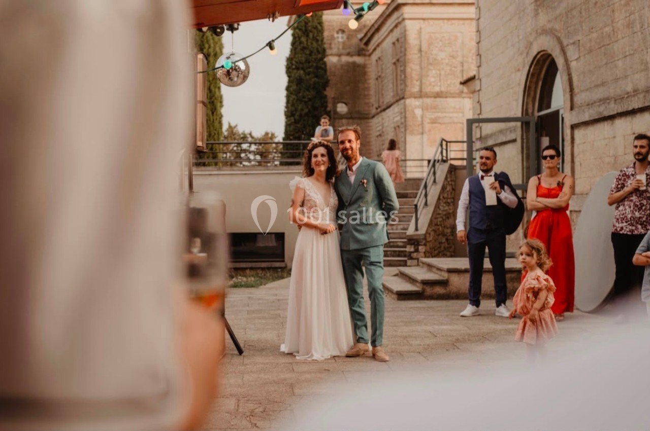 Un couple en tenue de mariage pose à l'extérieur, entouré d'invités dans une ambiance festive.