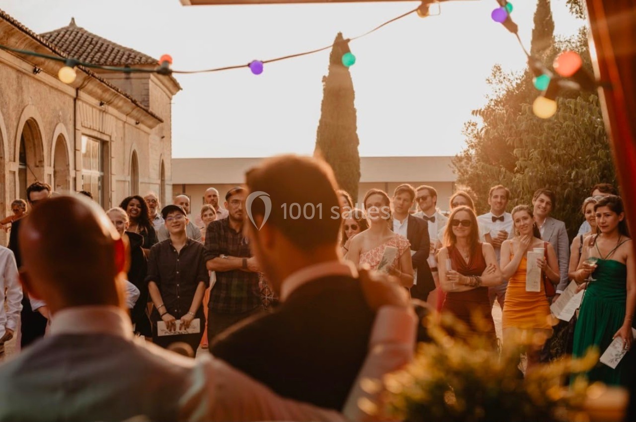 Un groupe de personnes assiste à un événement en extérieur au coucher du soleil, décoré de guirlandes lumineuses.