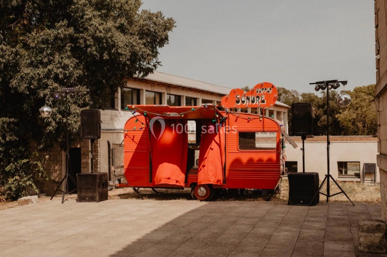Caravane rouge aménagée en scène sonore, entourée de haut-parleurs, installée en extérieur près de bâtiments.