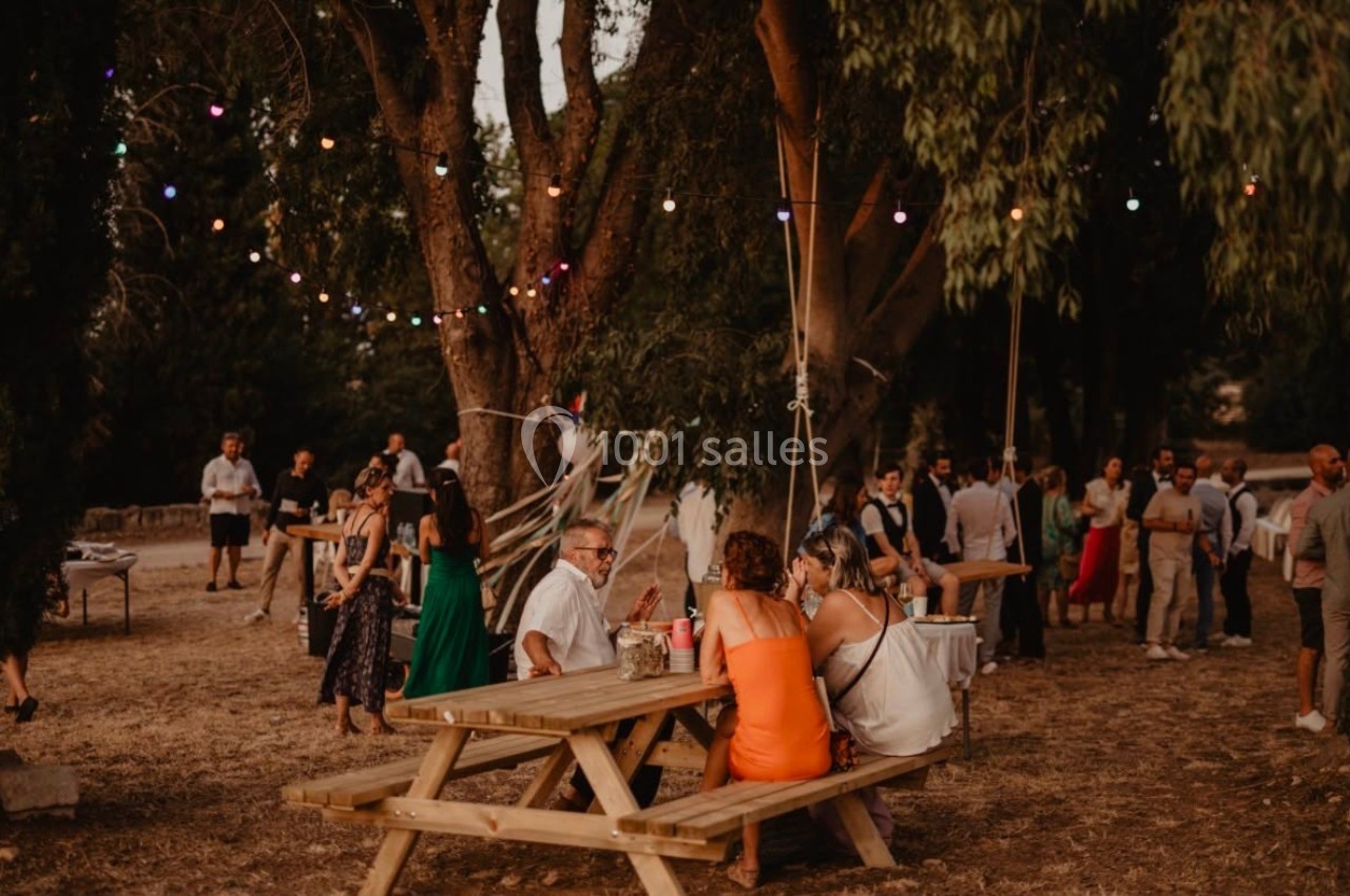 Des personnes discutent autour d'une table en bois lors d'un événement en plein air avec des guirlandes lumineuses.