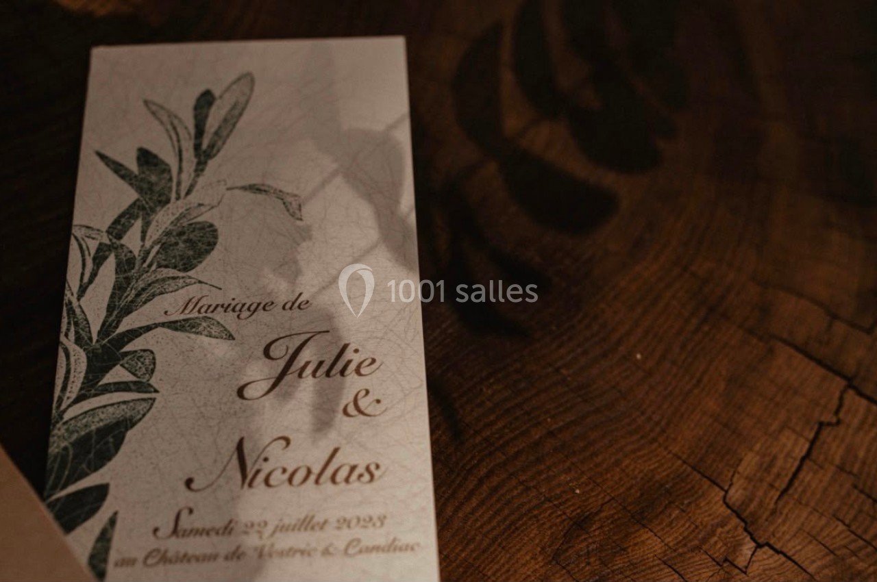 Faire-part de mariage posé sur une table en bois, avec des motifs végétaux et des inscriptions manuscrites.
