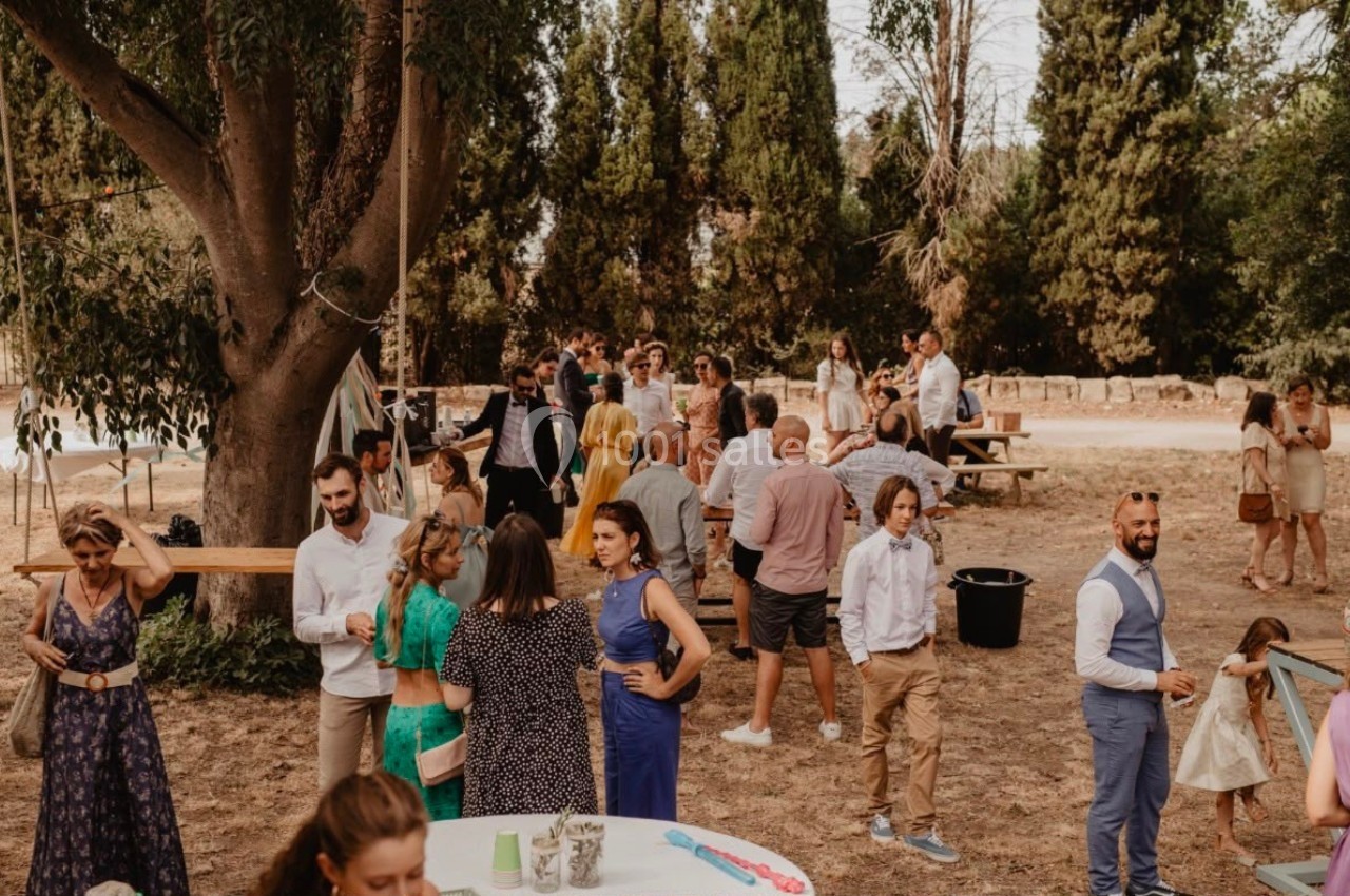 Groupe de personnes discutant dans un jardin lors d'un événement en plein air, entouré d'arbres et de tables.