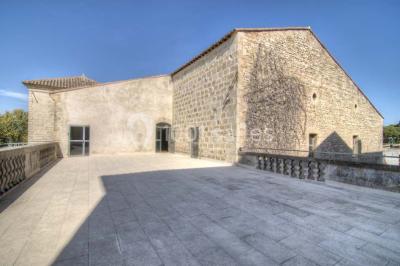 Terrasse en pierre spacieuse devant un bâtiment ancien en pierre sous un ciel bleu dégagé.