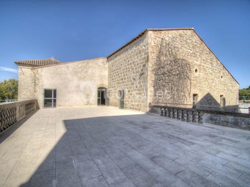 Terrasse en pierre spacieuse devant un bâtiment ancien en pierre sous un ciel bleu dégagé.