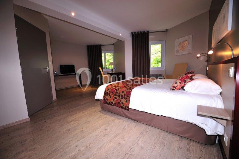 Chambre spacieuse avec lit double, parquet, bureau, télévision, grandes fenêtres et rideaux sombres.