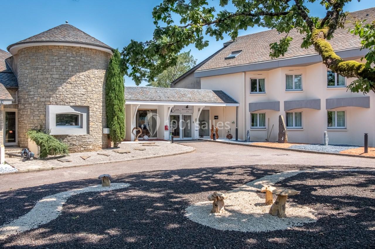 Entrée d'un bâtiment moderne avec façade en pierre et crépi, entouré d'arbres et d'un aménagement paysager.
