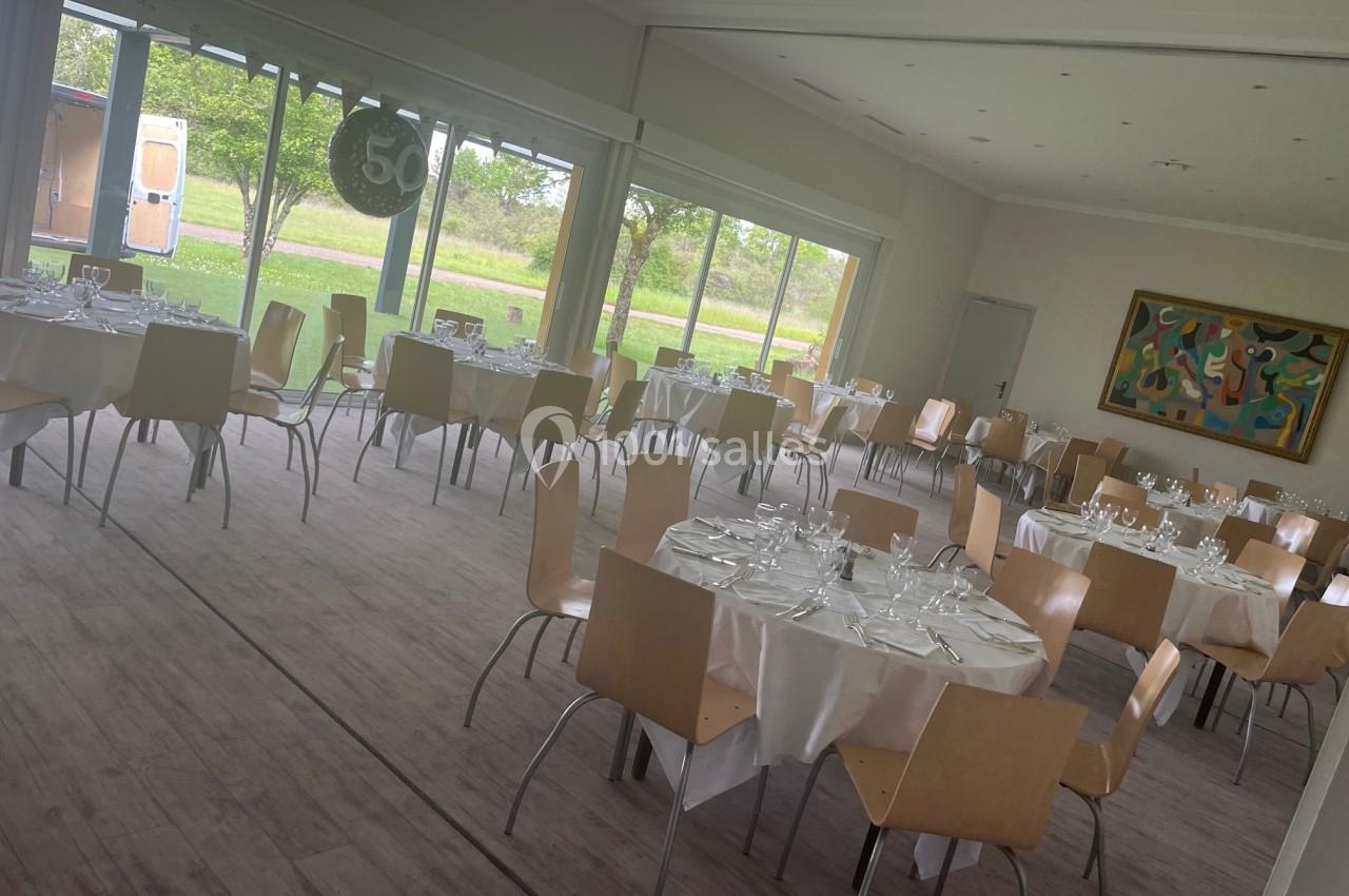 Salle lumineuse avec des tables rondes dressées pour un repas, chaises en bois clair et vue sur un espace extérieur…