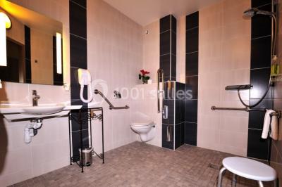 Salle de bain accessible avec douche à l'italienne, barres d'appui, lavabo adapté et toilettes surélevées.