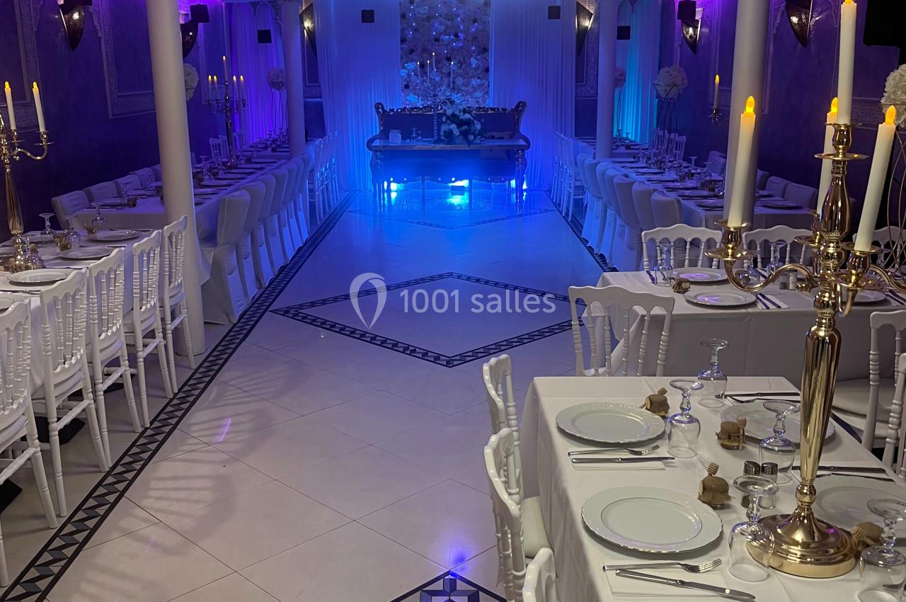 Salle de réception élégante avec tables dressées, chandeliers dorés et éclairage d'ambiance violet et bleu.