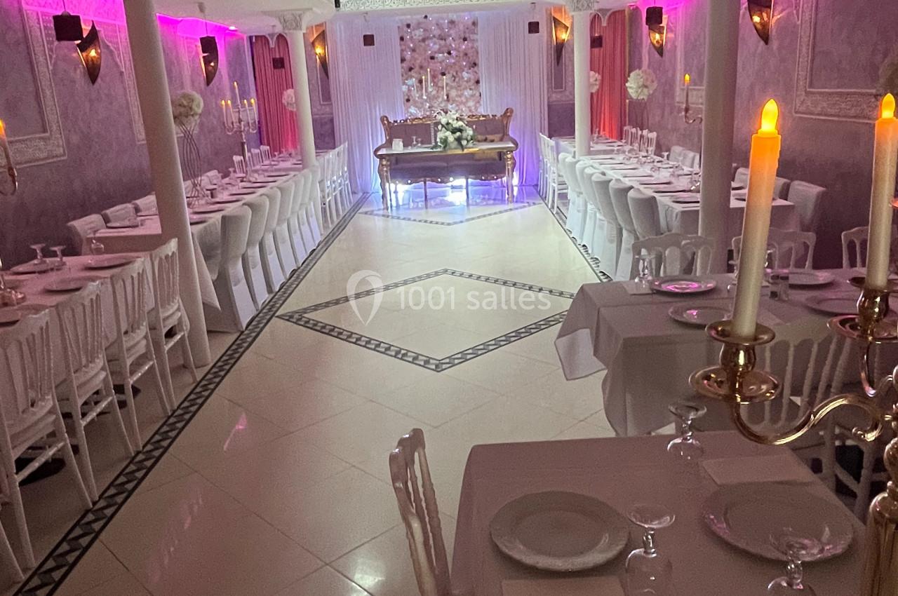Salle de réception décorée avec des tables dressées, des chandeliers et un éclairage rose tamisé.