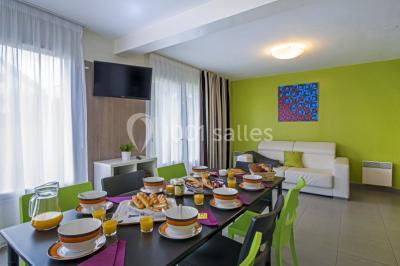 Salle de réunion lumineuse avec tables en U, chaises noires, grandes fenêtres donnant sur un jardin verdoyant.