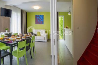 Salle de réunion lumineuse avec tables en U, chaises noires, grandes fenêtres donnant sur un jardin verdoyant.