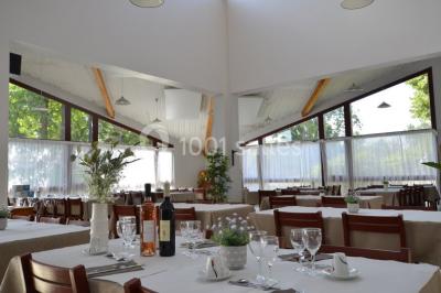 Salle de réunion lumineuse avec tables en U, chaises noires, grandes fenêtres donnant sur un jardin verdoyant.