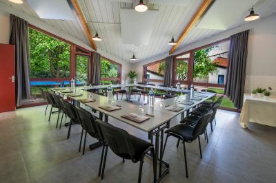 Salle de réunion lumineuse avec tables en U, chaises noires, grandes fenêtres donnant sur un jardin verdoyant.