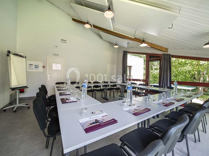 Salle de réunion lumineuse avec tables disposées en U, chaises, paperboard et vue sur un espace extérieur verdoyant.