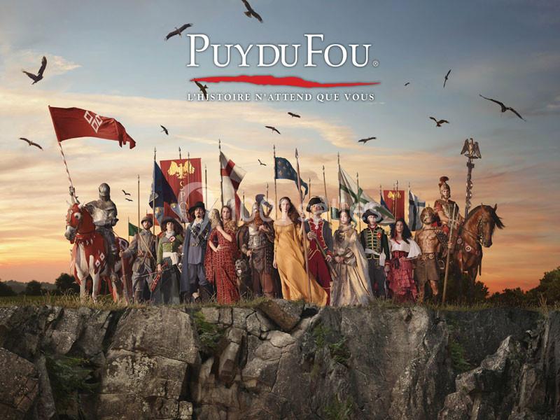 Groupe de personnages costumés représentant différentes époques historiques, debout sur une falaise au coucher du soleil.