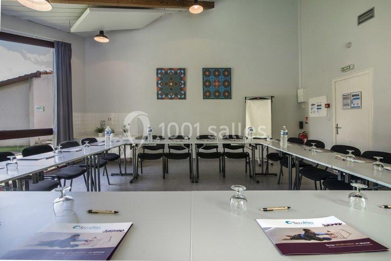 Salle de réunion lumineuse aménagée en U, avec chaises, tables, bouteilles d'eau et documents posés.