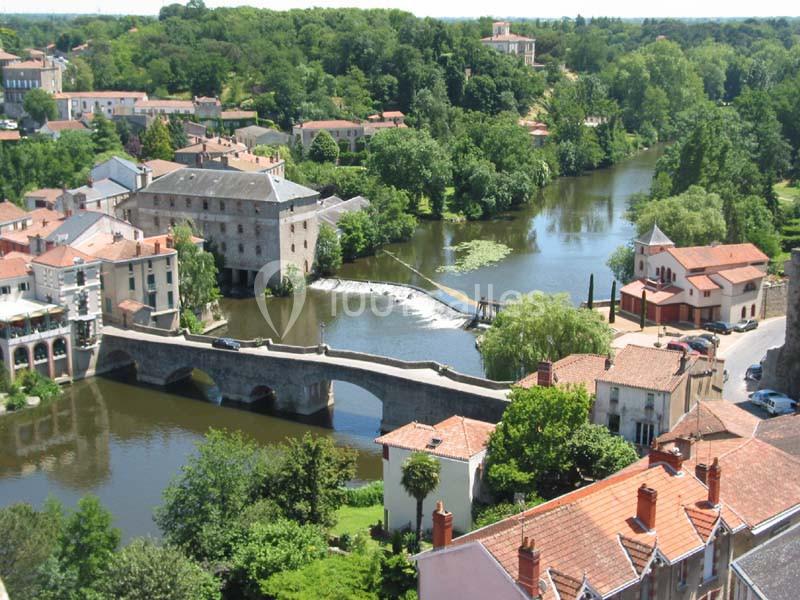 Vue aérienne d'un village avec un pont en pierre traversant une rivière entourée de bâtiments et de végétation.