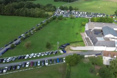 Chambre mansardée avec lit double, poutre apparente, télévision murale, commode, chaise et lampe de chevet.